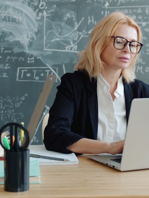Lehrerin arbeitet am Laptop vor einer Tafel mit Formeln – Symbolbild für den Workshop „KI im Unterricht